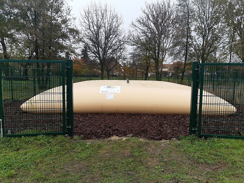 Eine große, gelbe, faltbare Zisterne, die eingezäunt auf einer Wiese aufgestellt ist. Zisternen sind Behälter, in denen Wasser gespeichert wird.