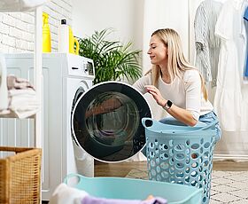 Bild zeigt eine Waschmaschine, Frau belädt die Waschmaschine mit Wäsche 