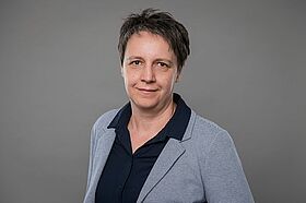 Portrait von Jana Bräutigam, Prokuristin und Leiterin Projektentwicklung der MIDEWA vor einem grauen Hintergund. Frau Bräutigam trägt eine schwarze Bluse und ein graues Sakko. 