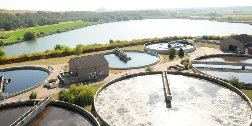 Ein Luftbild der Kläranlage Rollsdorf. Es zeigt verschiedene runde Becken der Abwasserbehandlungsanlage (Belebungsbecken, Vorklärbecken) und zwei technische Gebäude auf dem Gelände.