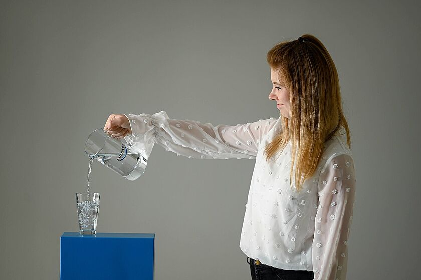 Kundenservice Mitarbeiterin im MIDEWA-Kundencenter gießt Trinkwasser in ein Glas.
