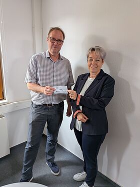 Ein MIDEWA-Mitarbeiter und die Bürgermeisterin Christina Buchheim stehen nebeneinander und halten gemeinsam das gezogene Los in die Kamera. Gezogen wurde die Stadt Arnstein.